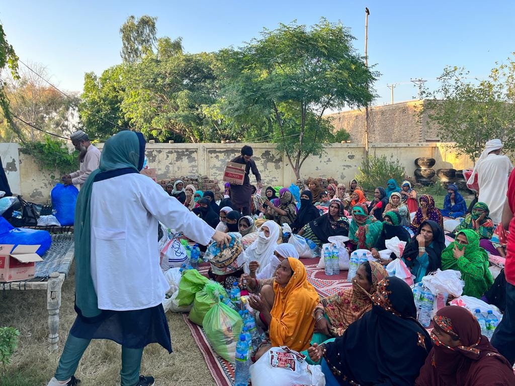 A Muslim Medical Mission doctor distributing relief supplies to women waiting in a courtyard